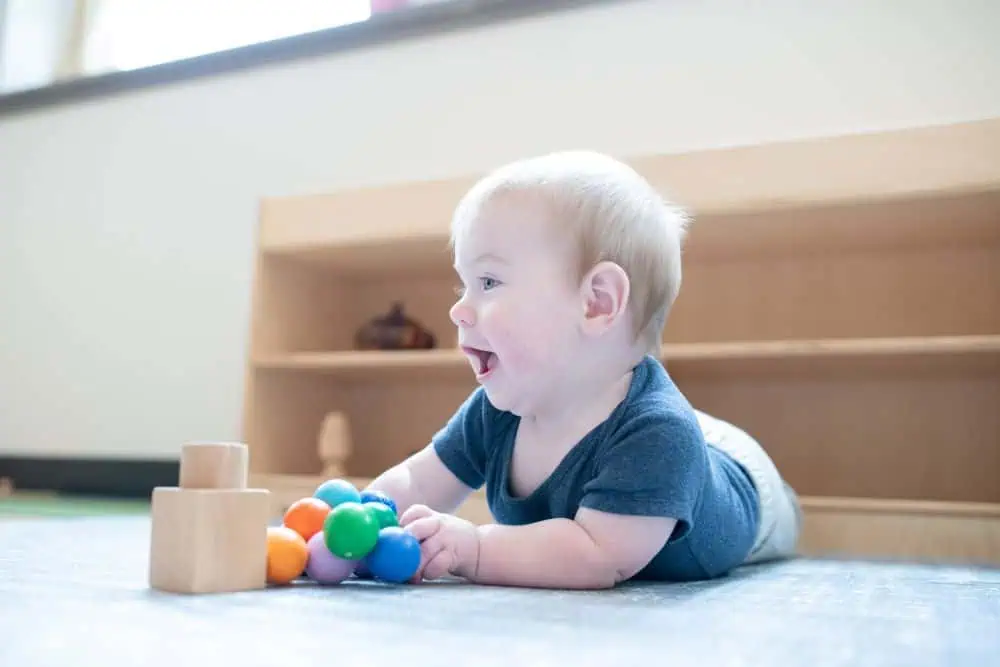 Infant doing tummy time on the daycare floor playing with wood Montessori toys
